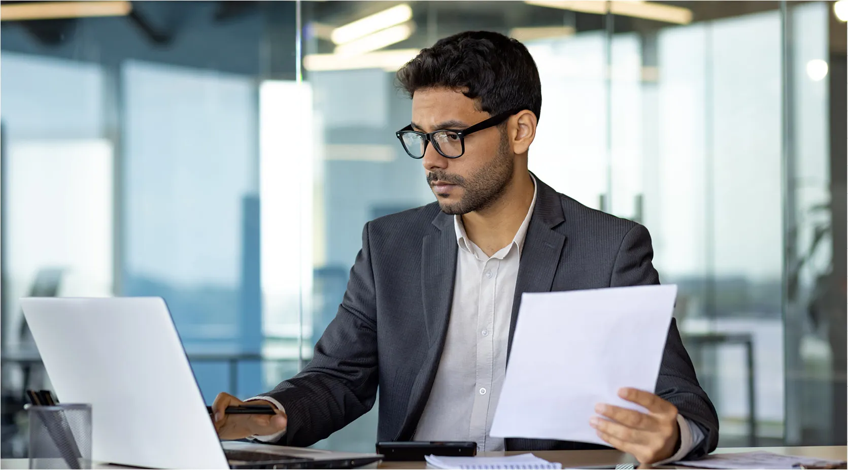 Man in suit reviewing documents and laptop, business compliance