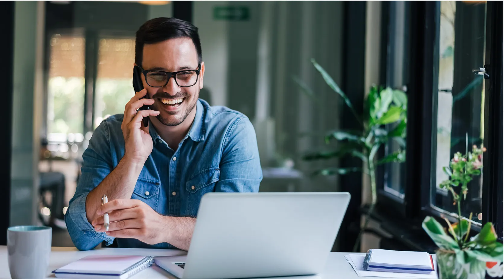 Man on phone at desk with laptop, discussing digital quality management.