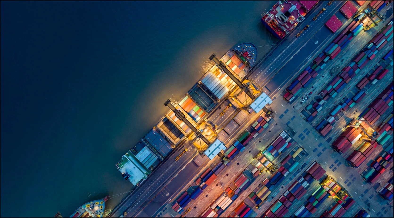 Aerial view of a busy, illuminated shipping port at night with cargo ships and containers.