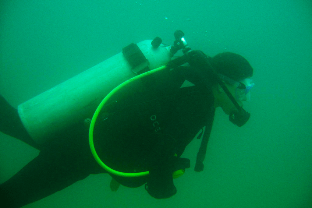 Scuba diver in dark wetsuit with bright green air hose in green underwater visibility