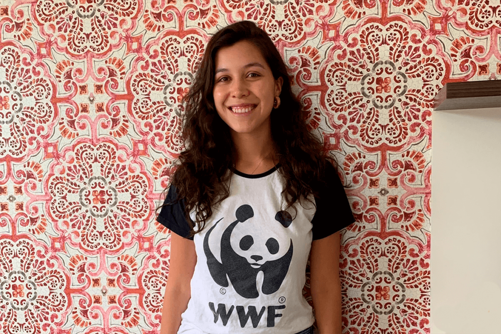 Young woman in WWF shirt smiles in front of patterned wallpaper