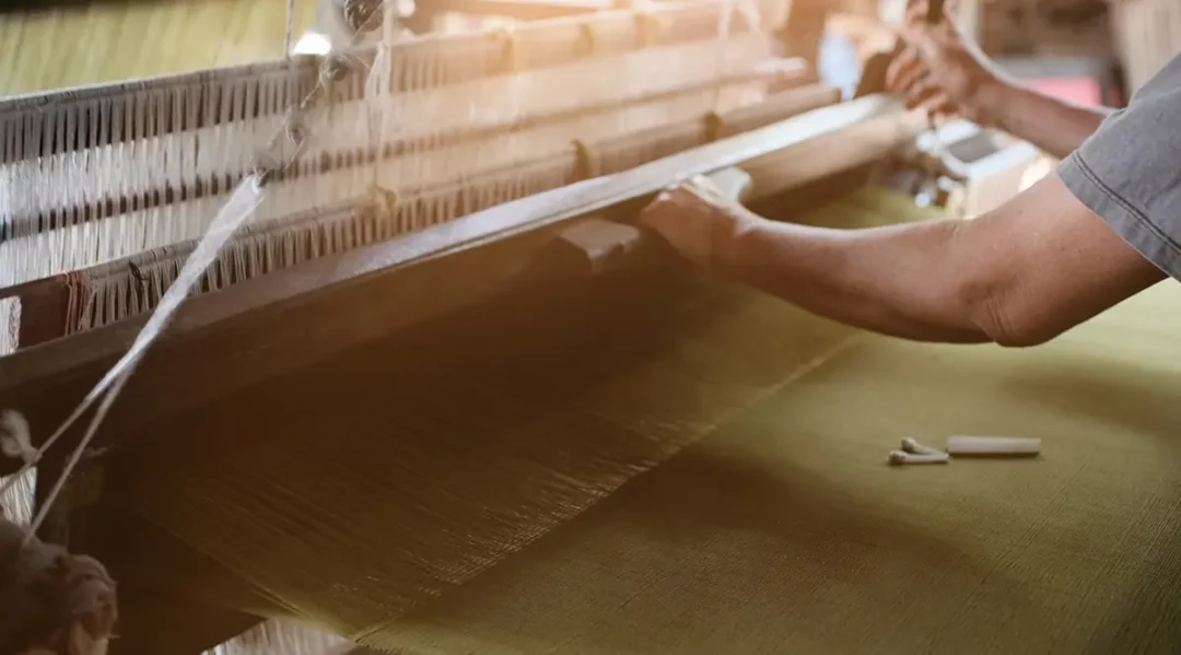 Hands operating a traditional loom, weaving fabric for supply chain due diligence.