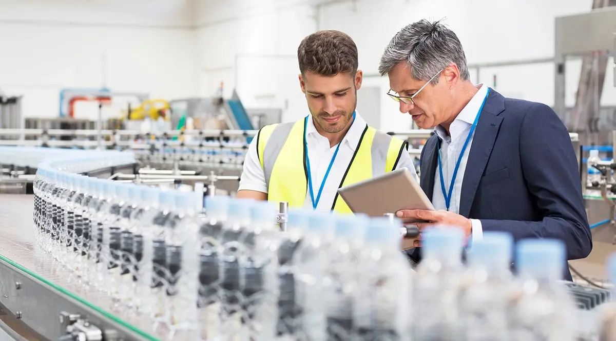 Factory managers review quality control data on a tablet on a bottling line.