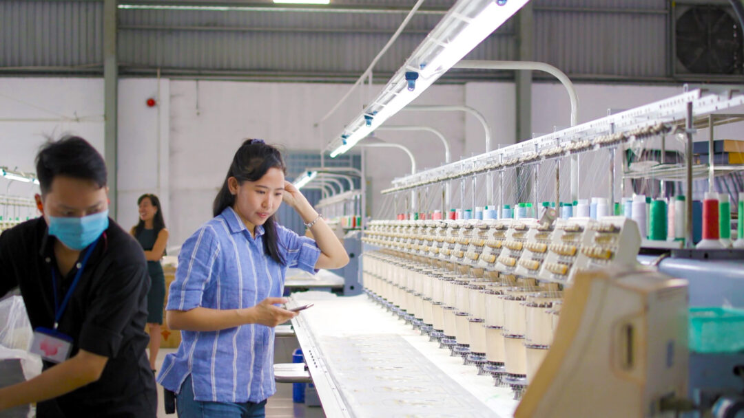 Workers in a garment factory inspect embroidery machines, optimizing supply chain management.
