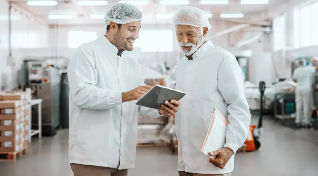 Supply chain managers review data on a tablet in a clean production facility.