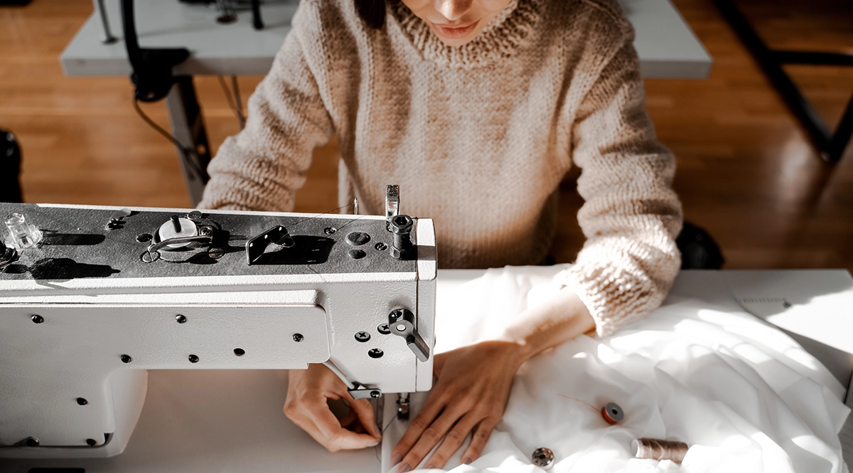 Woman sewing white fabric on a sewing machine, luxury apparel compliance