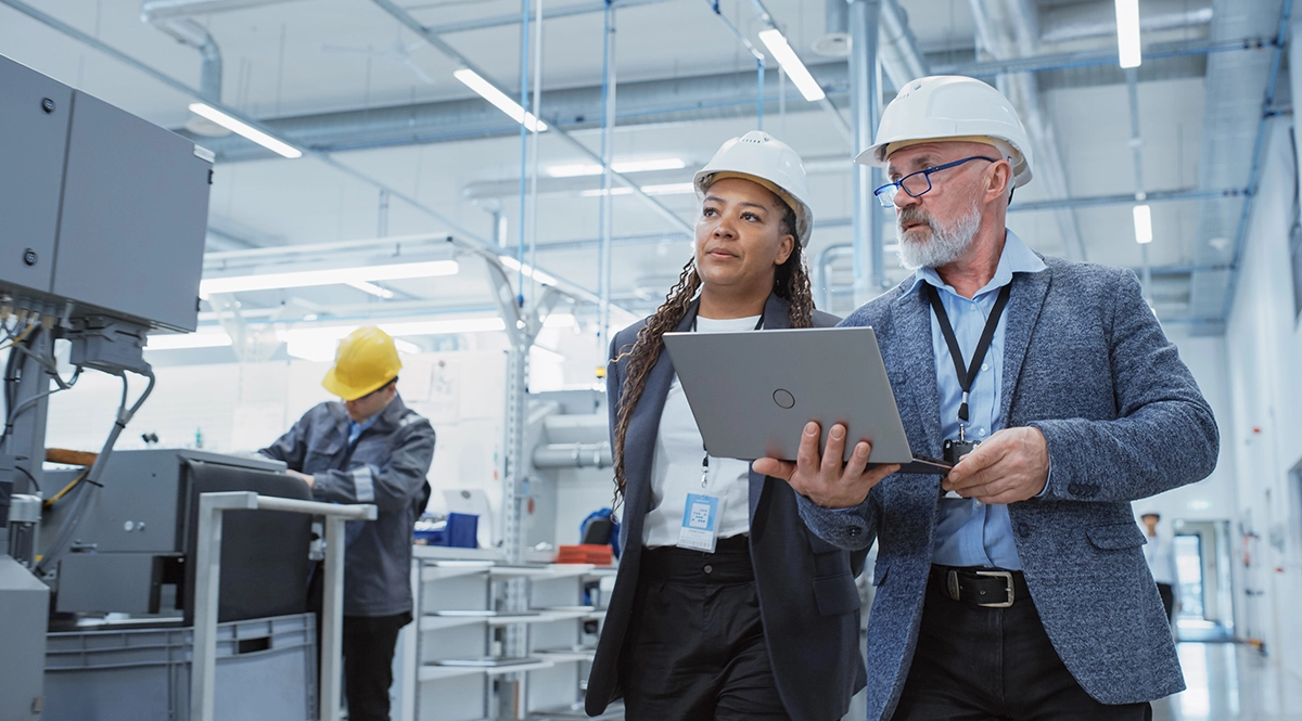 Engineers in hard hats review data on a laptop in a modern factory.