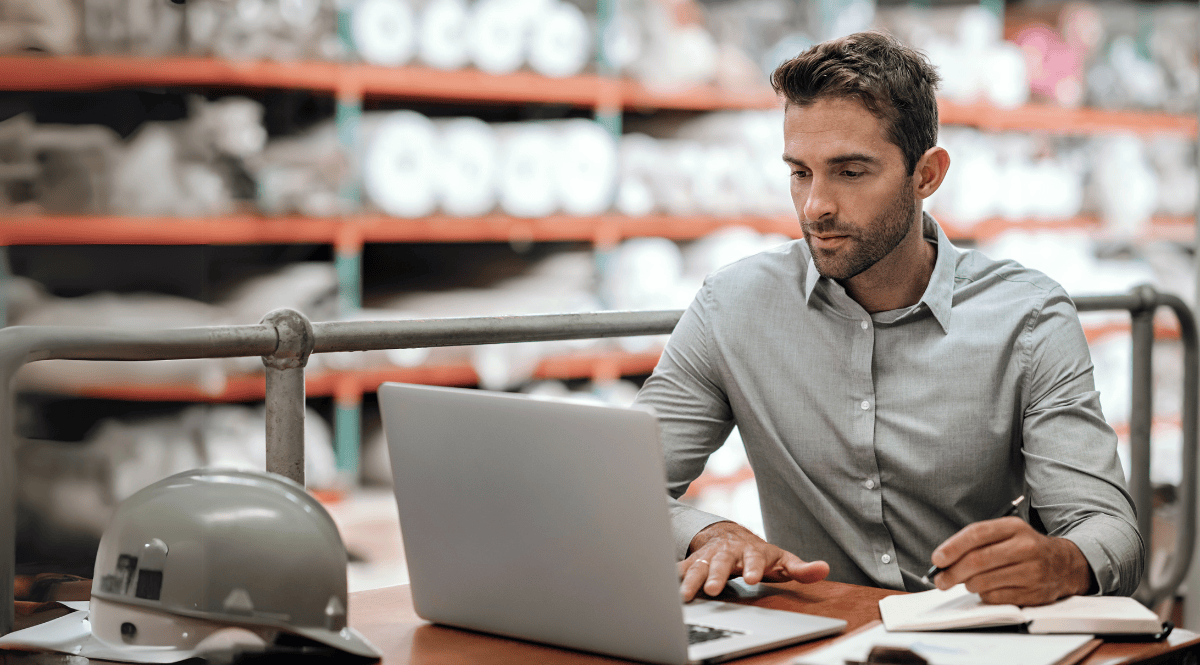 Man in warehouse using laptop for supply chain risk management.